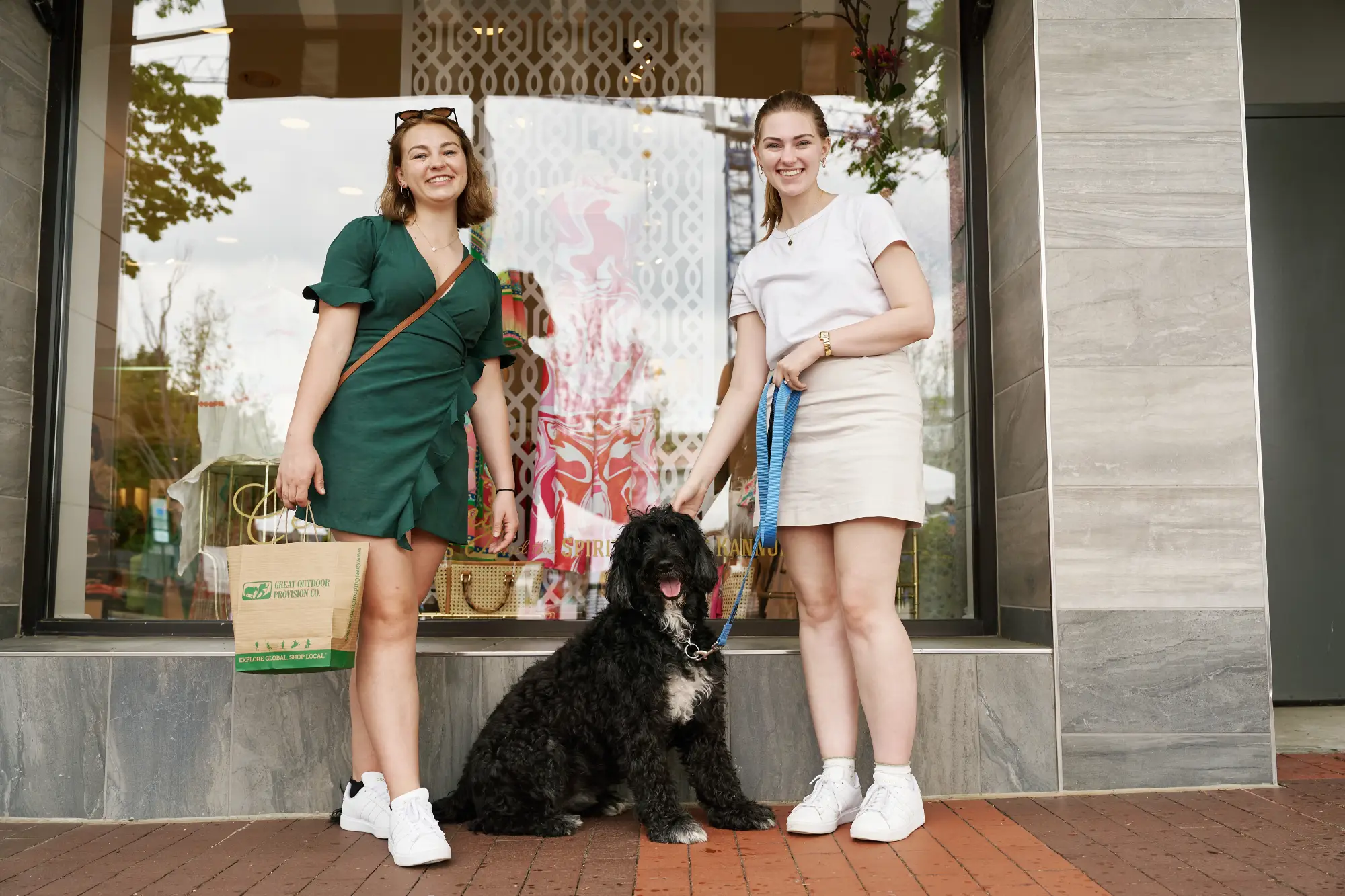 two girls smiling with a black dog