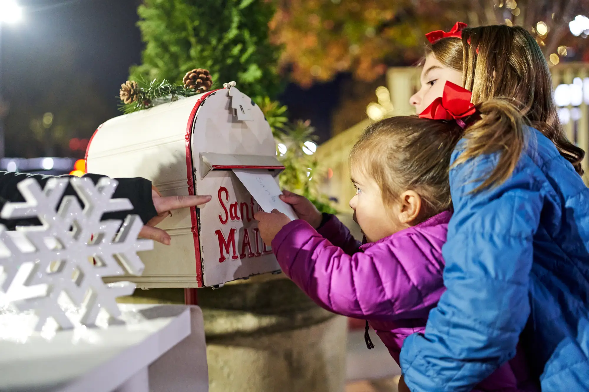 an older little girl lifting a small little girl to put Santa's letter in the mailbox
